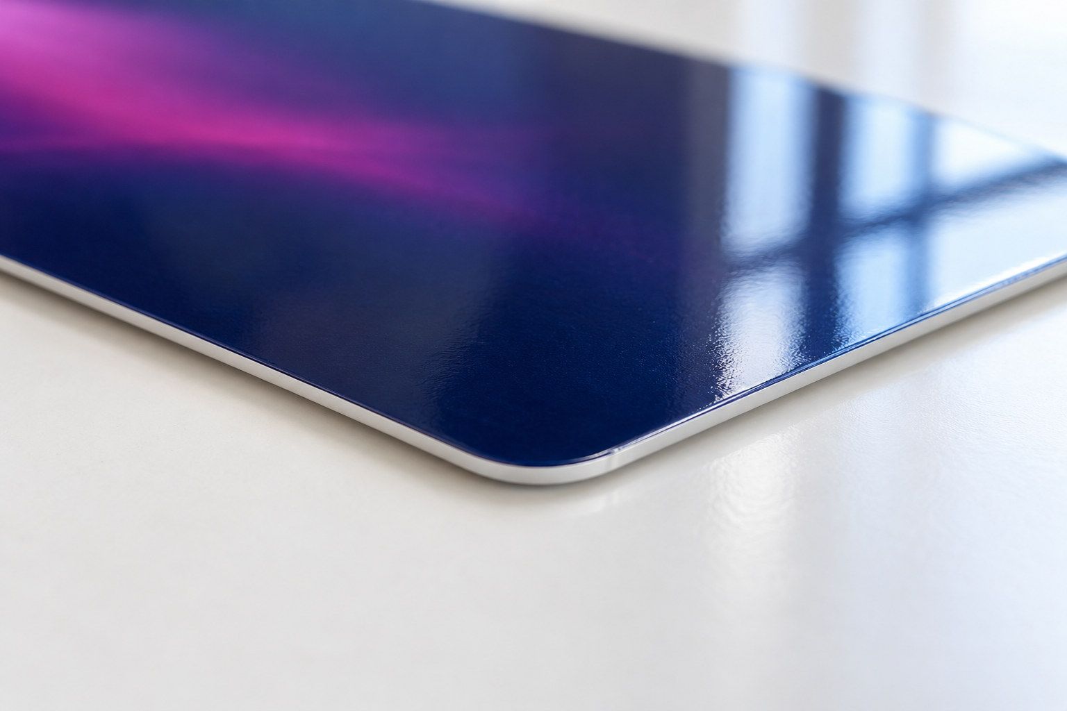 Illustration of the rounded corner of a glossy dark blue plastic card on a white desk, showing its thin white edge and a window reflected in its surface