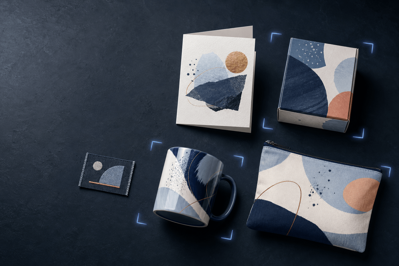 A flat-lay of finished printed products, a folded card, mailer box, coffee mug, zip pouch and woven patch, all sharing one blue, cream and copper print design, framed by blue registration brackets on a dark slate surface